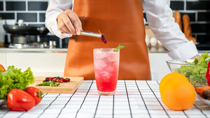 Asian housewife using a tongs to putting mulberry into cocktail in a glass while wearing apron