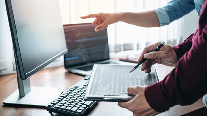 Team of asian programmer holding pen to pointing code data on document and pointing on laptop screen