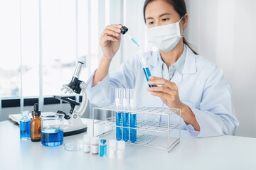 Fototapeta premium Scientist woman in medical face mask is analyzing with microscope and using dropper to dropping solution