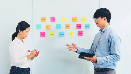 Two business executive team holding and taking notes keyword on board wall to brainstorm about a...