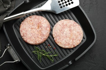 Fresh raw patties for burger and spices in frying pan on black table, top view