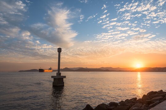 Santos city, Brazil. Colorful sunset in the bay. The Portuguese Standard Monument in the foreground and a cargo ship entering the Santos port channel.