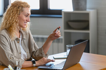 Fototapeta premium Woman using a credit card for online shopping at home, sitting at a desk with a laptop, focused on making a secure digital payment.
