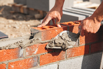 Close-up of Skilled worker laying bricks with trowel on construction site