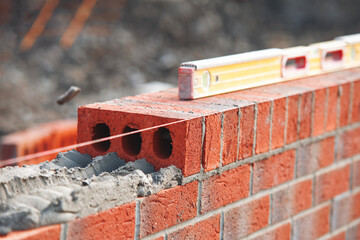 Close-up of skilled bricklayer working on construction site laying red bricks for wall construction while