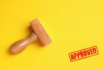 Red stamp Approved and wooden stamp on yellow background, top view