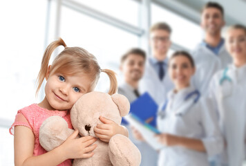 Cute child holding toy bear and medical staff in hospital. Pediatric ward