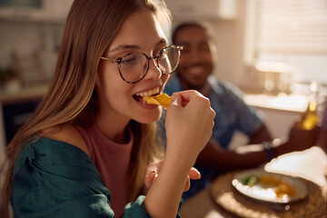 Young woman having nachos while eating with friends at dining table.