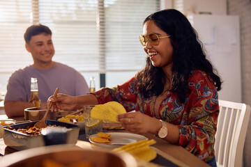 Happy Indian woman eating tacos during lunch party with friends.
