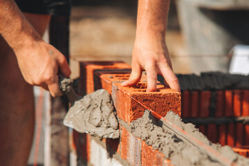 Construction worker bricklayer lays bricks for new structure at building site using tools and...