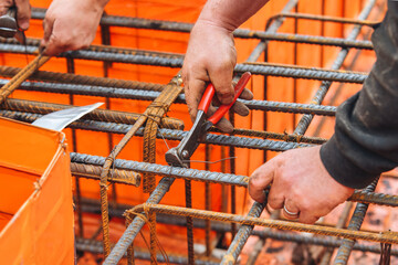 Close-up of steel fixer construction worker assembling rebar for concrete foundation on building site