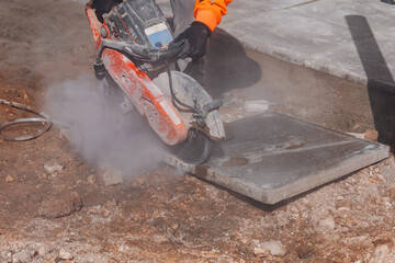 Builder cutting concrete paving slab with petrol concrete saw and a diamond blade during external footpath paving works close up