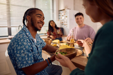 Happy black man eating tacos during lunch party with friends at home.