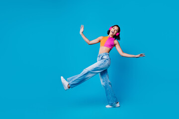Obraz premium Young stylish woman enjoying music and dancing with headphones against a vibrant blue background