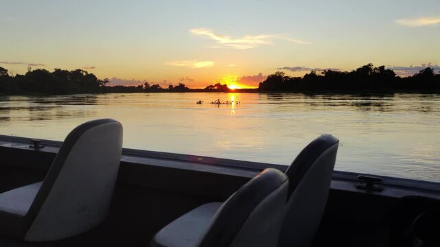Timelapse of scenic sunrise or sunset over the calm waters of the Cuiab&aacute; River in the Pantanal wetlands, viewed from a boat, with golden reflections, lush vegetation, and peaceful natural surroundings