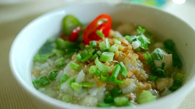 Authentic Asian style breakfast featuring a hot bowl of congee with fragrant toppings and visible heat steam, shot in natural light.