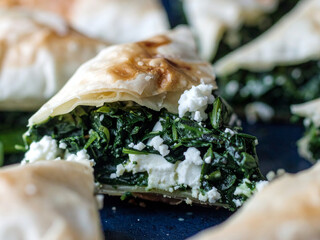 Crispy Greek spanakopita pastry filled with fresh spinach and feta cheese on a dark background.
