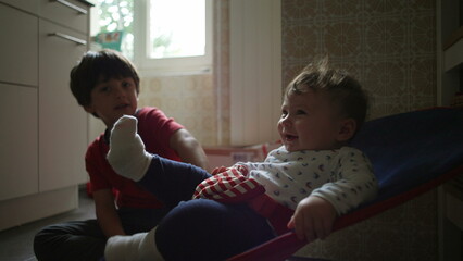 Baby in a bouncer looking up while big brother watches, curious sibling interaction in a cozy...