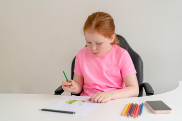Girl focuses on drawing with colored pencils at a white desk in a bright room during a calm afternoon
