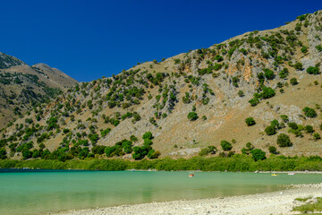 Clear turquoise waters of Lake Kournas with mountainous landscape under blue sky in Crete, Greece