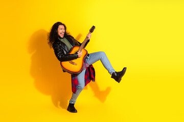 Obraz premium Young man playing guitar energetically in stylish outfit on vibrant yellow background, expressing joy and music passion