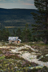 An isolated abandoned log cabin on a mountain slope stands in Idre Dalarna, Sweden, offering a breathtaking view of the surrounding boreal forest and majestic mountains at dusk