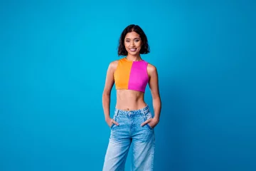 Fotobehang Attractive young woman posing confidently in a vibrant outfit with a blue background perfect for fashion or lifestyle themes © deagreez