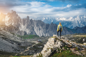 Young woman hiker with backpack standing on a rock in majestic mountain valley with high alpine...