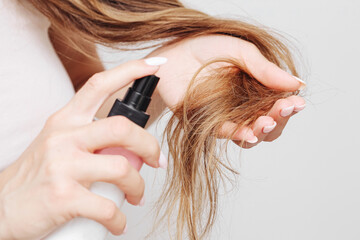 Haircare spray application. Woman using mist on hair ends. White background and natural look. Healthy beauty routine at home. Close-up female hands and bottle. Smooth strands and selfcare ritual.