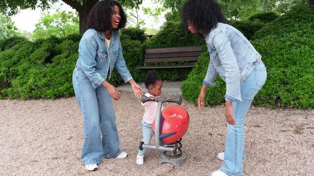 African mother and aunt enjoying leisure time with niece, playing together on seesaw in a playground, having fun on a sunny day