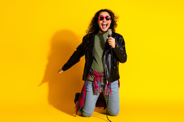Obraz premium Energetic young man singing with enthusiasm in a vibrant yellow background wearing trendy clothing and style