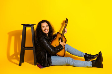 Young man in a black leather jacket playing guitar on a vibrant yellow background, exuding...
