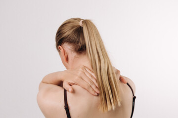 Fototapeta premium Young woman with long blonde hair is experiencing neck pain while gently massaging her shoulder, showcasing a moment of discomfort and self-care in a serene indoor environment with soft lighting