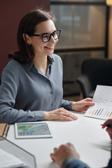 Vertical portrait of smiling businesswoman wearing glasses while enjoying work meeting with colleague in office