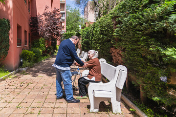 Male Family assisting an elderly woman in standing up from a bench in a nursing home's garden, fostering comfort and dignity in care
