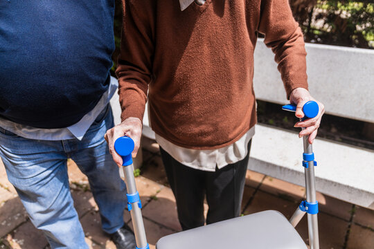 Family helping elderly woman using a walker in the garden of a nursing home, providing support and care for senior mobility