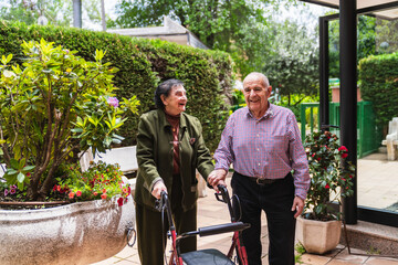 Happy elderly couple using walkers in the garden of a retirement home, enjoying time together and each other's company