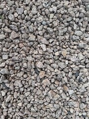 Top-down view of small crushed granite gravel stones in varying shades of gray and pink, with a...