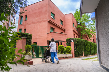 Nurse assisting elderly person in a wheelchair, navigating the grounds of an outdoor nursing home, emphasizing senior care and mobility