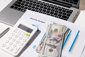 A monthly budget graph paper is placed on the desk alongside a calculator, laptop, and...