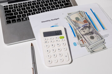 A monthly budget graph paper is placed on the desk alongside a calculator, laptop, and...