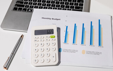 A monthly budget graph paper is placed on the desk alongside a calculator, laptop, and...
