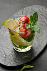 Refreshing mojito cocktail with lime, mint, strawberry, and ice on dark background