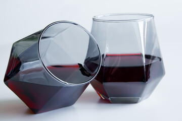 Two geometric stemless tinted whiskey glasses balancing on their edges filled with dark liquid, ideal for showcasing modern barware in luxury beverage advertising. Photo