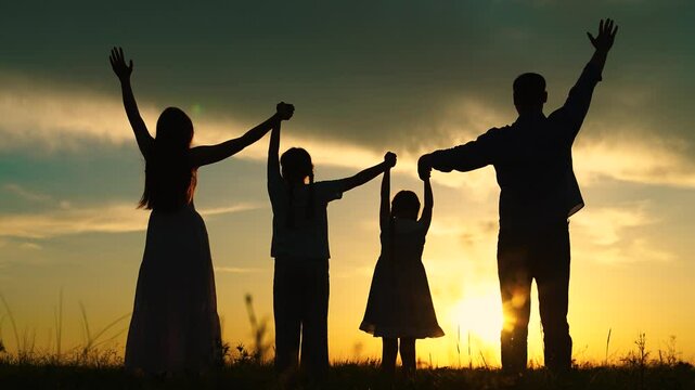Cheerful happy family team raising hands in nature, silhouette of parents children. Mom dad daughters standing with raised hands against sky, teamwork. Family prayer in nature, holding hands in park