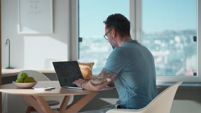 Man with CGM sensor on arm sitting at table and working on laptop.