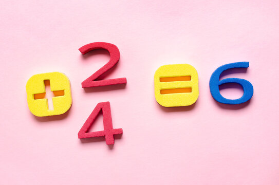 Addition equation with foam colorful numbers on pink background.