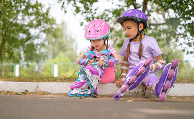 Cute little girls putting on roller skates sitting on the sidewalk. Active sports during the summer holidays