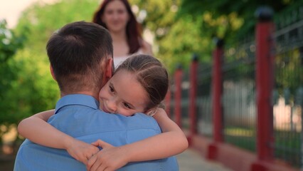 Fototapeta premium Loving father tenderly embraces his daughter in summer park day outdoor. Happy family closeup, dad hugs his child girl on walk in city park with green trees. Happy childhood, happy family kid girl mom