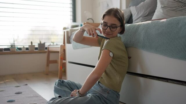 Diabetic girl with CGM sensor checking her blood sugar in app.